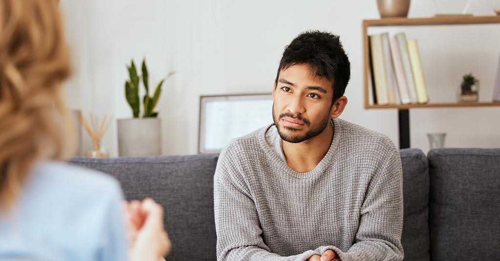 Female transactional analyst and Asian man sitting and talking during a mental health therapy session.