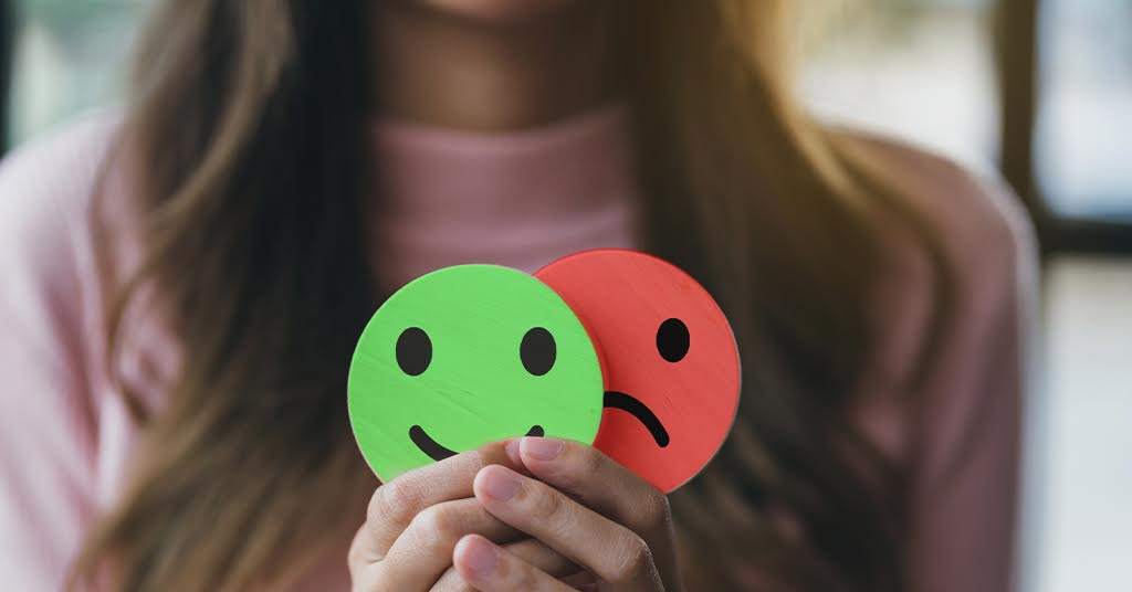 Woman holding a red circular smiley face in front of green circular sad face, demonstrating the benefits of Cognitive Behavioural Therapy