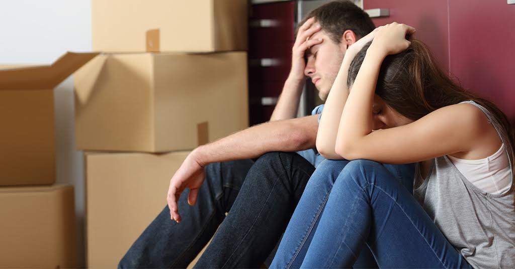 Relocation and mental health: a couple with heads in their hands sitting next to boxes