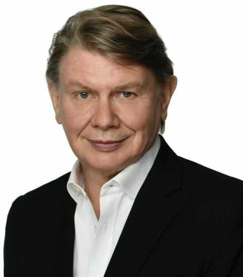 Eric Wishart: a man with short dark hair, wearing a suit and tie, smiling at the camera. Background features a neutral, professional setting.