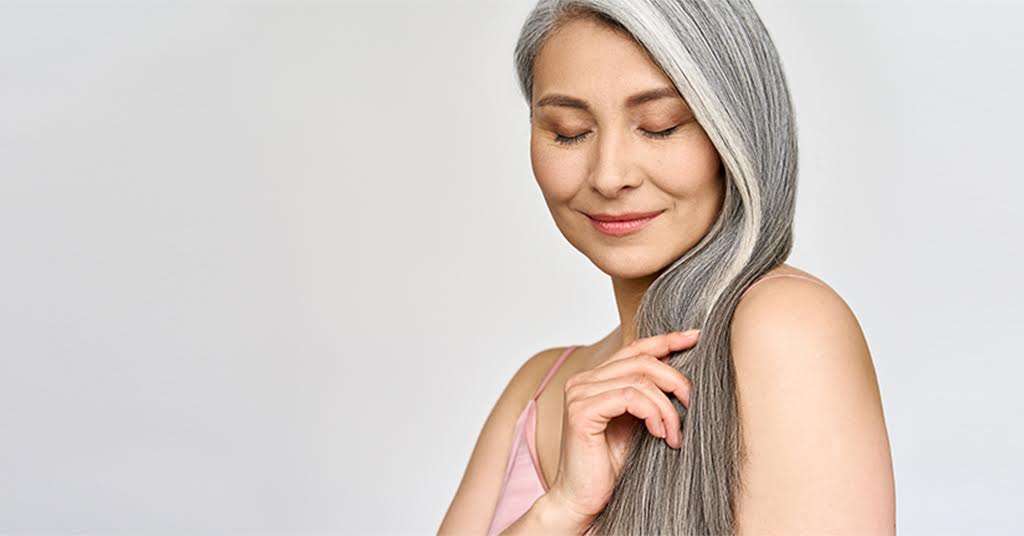 A woman smiles while holding her hair, symbolizing confidence and embracing the changes of menopause and healthy aging.