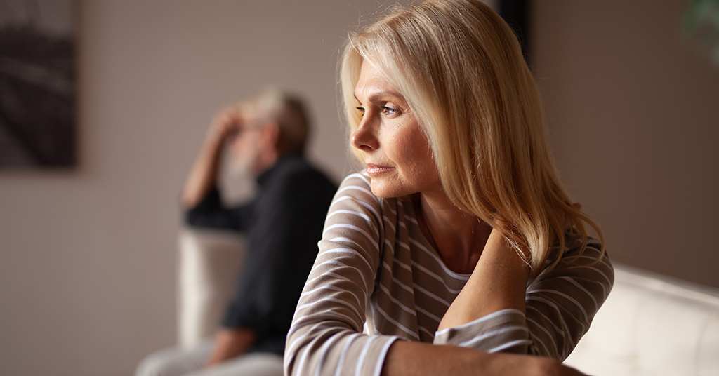 A couple sits in the same room, visibly upset, facing opposite directions, illustrating tension and conflict in their relationship.