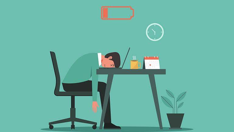 A man with his head resting on his work desk, looking exhausted, symbolizing fatigue and burnout.