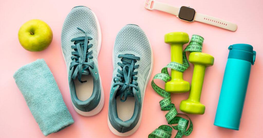 A flat lay composition featuring various fitness and health-related items arranged on a pastel pink background.